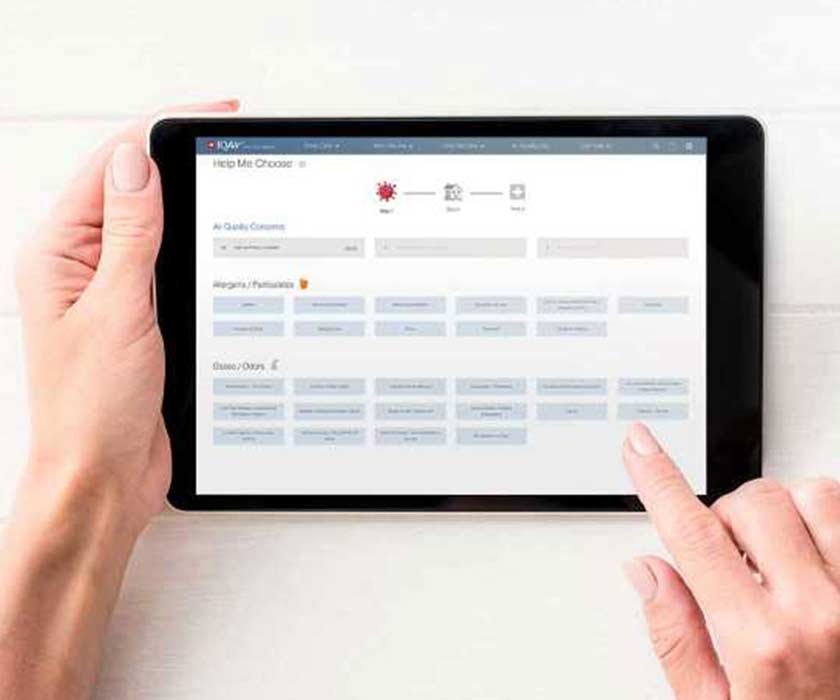 Hands holding a tablet with IQAir's 'Help Me Choose' tool to help users select air quality concerns and features to find the best air purifier. 